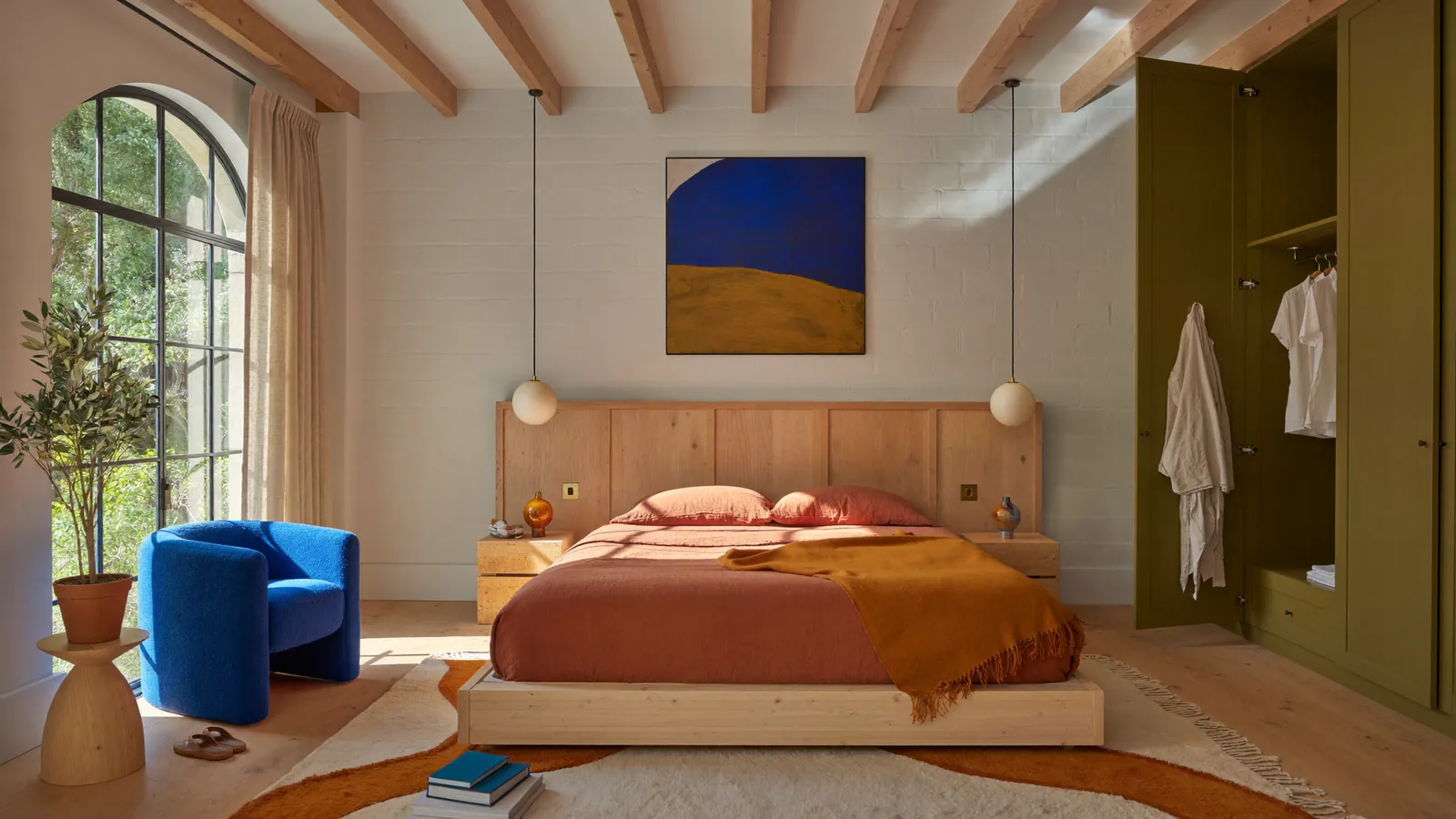 Camera da letto con testiera in legno, coperta arancione e poltrona blu